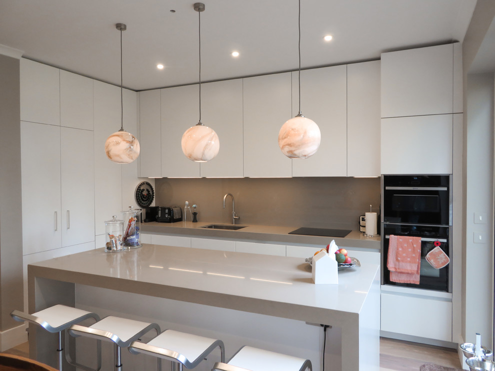 This is an example of a mid-sized modern l-shaped open plan kitchen in London with flat-panel cabinets, white cabinets, quartzite benchtops, glass sheet splashback, panelled appliances, ceramic floors and with island.