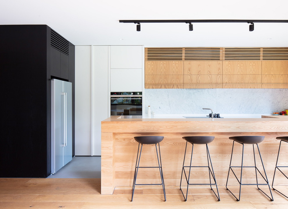 This is an example of a large contemporary l-shaped open plan kitchen in Melbourne with light wood cabinets, laminate benchtops, white splashback, stone slab splashback, with island, flat-panel cabinets and grey floor.