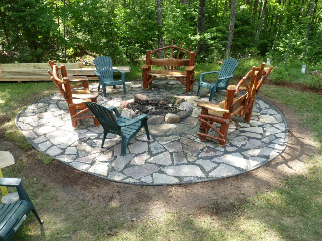 Example of a mountain style side yard stone full sun patio design for summer with a fire pit