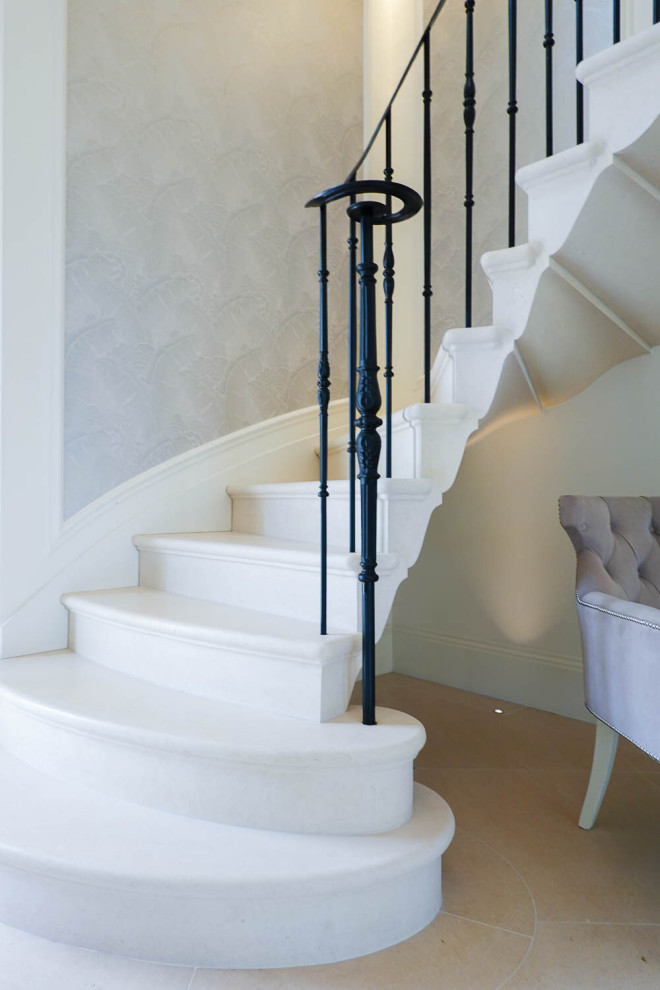 На фото: изогнутая лестница в классическом стиле с ступенями из известняка, подступенками из известняка и деревянными перилами