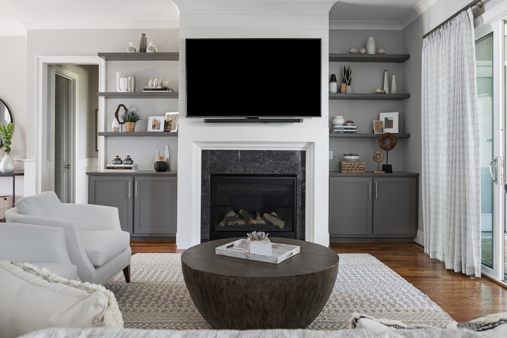 ローリーにある中くらいなトランジショナルスタイルのおしゃれなLDK (グレーの壁、淡色無垢フローリング、標準型暖炉、石材の暖炉まわり、壁掛け型テレビ、オレンジの床) の写真
