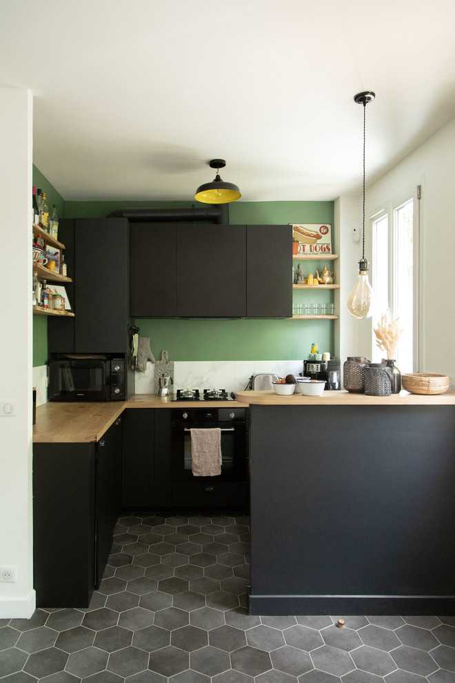Photo of a small industrial l-shaped eat-in kitchen in Other with white splashback, grey floor, beige benchtop, an undermount sink, flat-panel cabinets, black cabinets, wood benchtops, black appliances, cement tiles, a peninsula and marble splashback.