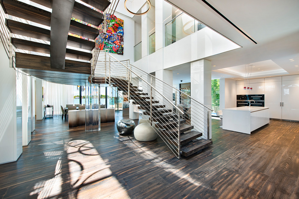 This is an example of an expansive contemporary wood curved staircase in Miami with open risers and cable railing.