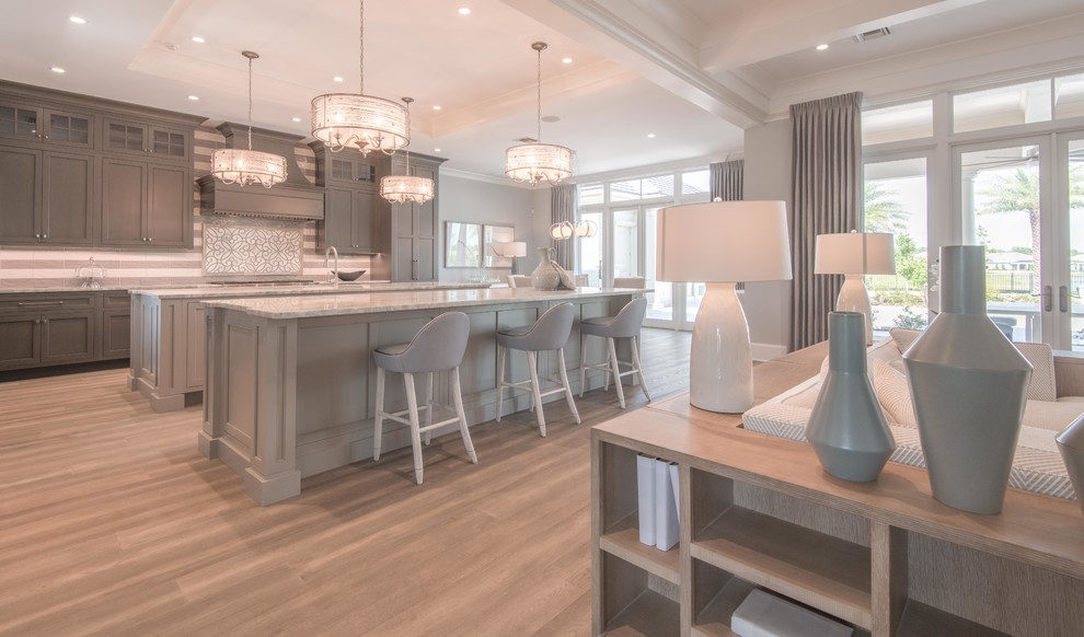 Expansive transitional l-shaped open plan kitchen in Tampa with an undermount sink, shaker cabinets, grey cabinets, marble benchtops, grey splashback, mosaic tile splashback, stainless steel appliances, light hardwood floors, multiple islands, grey floor and grey benchtop.