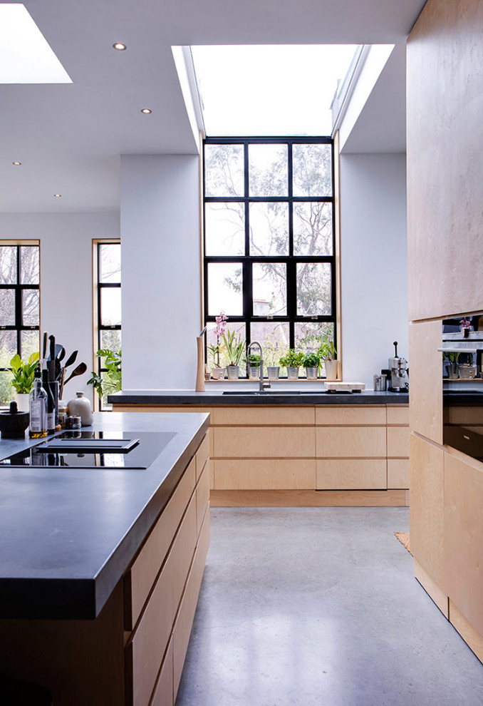 Inspiration for a mid-sized scandinavian eat-in kitchen in Dublin with a drop-in sink, flat-panel cabinets, light wood cabinets, concrete benchtops, concrete floors, with island and black benchtop.