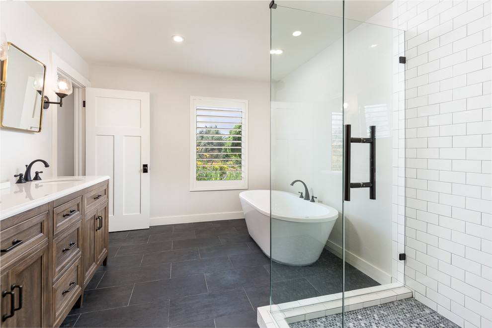 Mid-sized contemporary master bathroom in Dallas with recessed-panel cabinets, medium wood cabinets, a freestanding tub, a corner shower, white tile, subway tile, beige walls, porcelain floors, an undermount sink, solid surface benchtops, black floor, a hinged shower door and white benchtops.