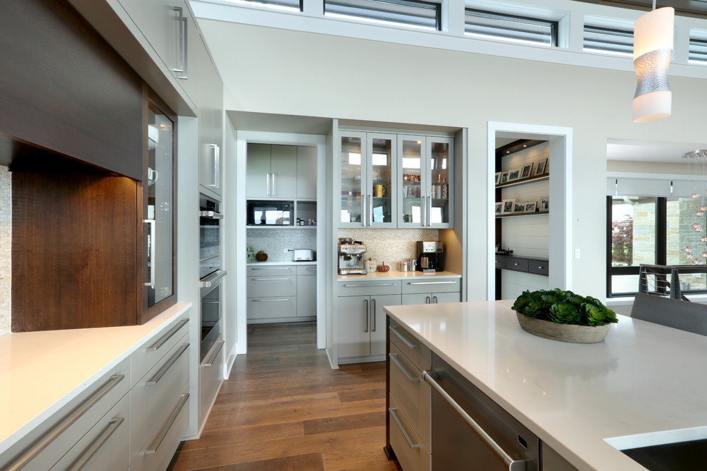 Eat-in kitchen - large contemporary l-shaped dark wood floor and brown floor eat-in kitchen idea in Grand Rapids with an undermount sink, flat-panel cabinets, gray cabinets, quartz countertops, metallic backsplash, glass tile backsplash, stainless steel appliances, an island and white countertops