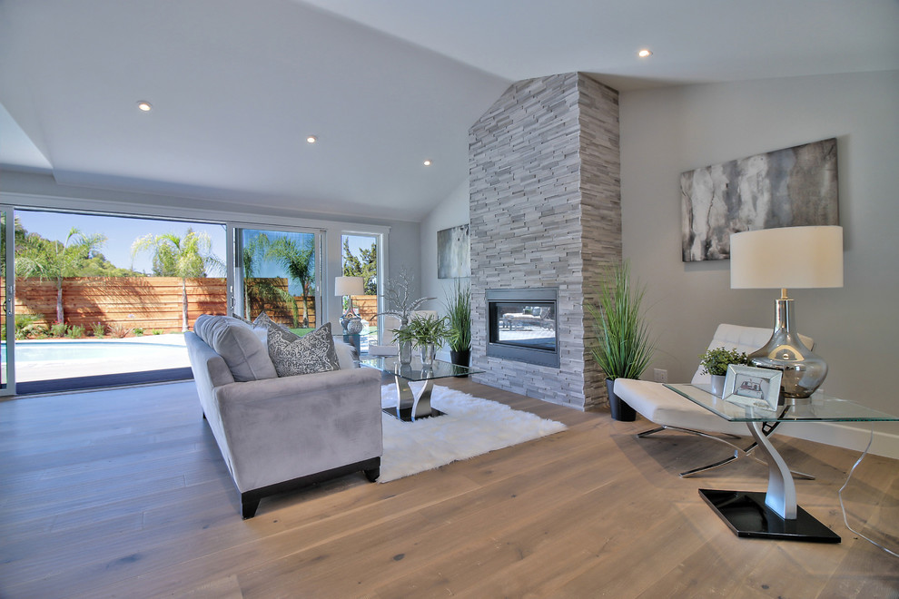 Photo of a modern open concept family room in San Francisco with grey walls, light hardwood floors, a standard fireplace, a stone fireplace surround and grey floor.