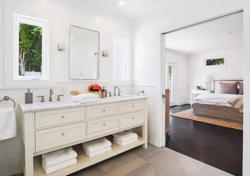 Design ideas for a medium sized traditional ensuite bathroom in Los Angeles with raised-panel cabinets, white cabinets, a freestanding bath, a corner shower, a one-piece toilet, white tiles, ceramic tiles, white walls, cement flooring, a submerged sink, marble worktops, grey floors, a hinged door, white worktops, double sinks, a freestanding vanity unit and wainscoting.