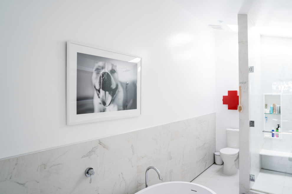 This is an example of a modern master bathroom in Los Angeles with a freestanding tub, a corner shower, a one-piece toilet, white tile, white walls, ceramic floors, marble benchtops, white floor and a hinged shower door.