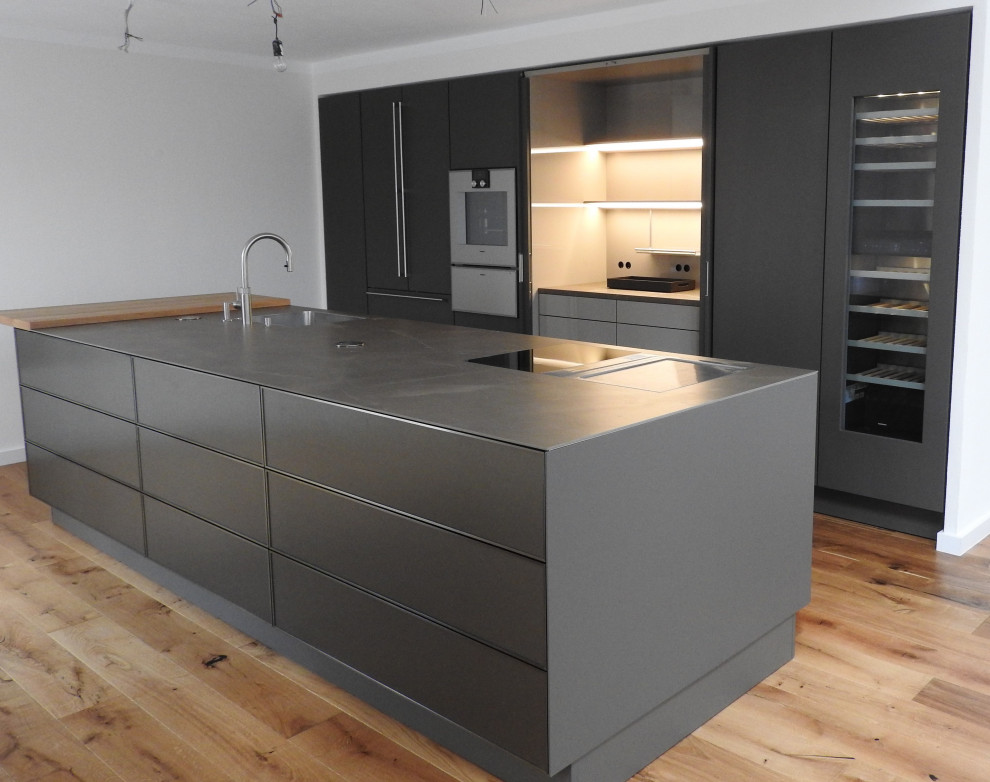 This is an example of a large modern single-wall open plan kitchen in Other with a drop-in sink, flat-panel cabinets, brown cabinets, solid surface benchtops, stainless steel appliances, light hardwood floors, with island and brown benchtop.