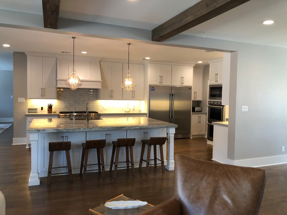 Open concept kitchen - large transitional l-shaped medium tone wood floor and brown floor open concept kitchen idea in Dallas with an undermount sink, shaker cabinets, white cabinets, quartz countertops, gray backsplash, ceramic backsplash, stainless steel appliances and an island