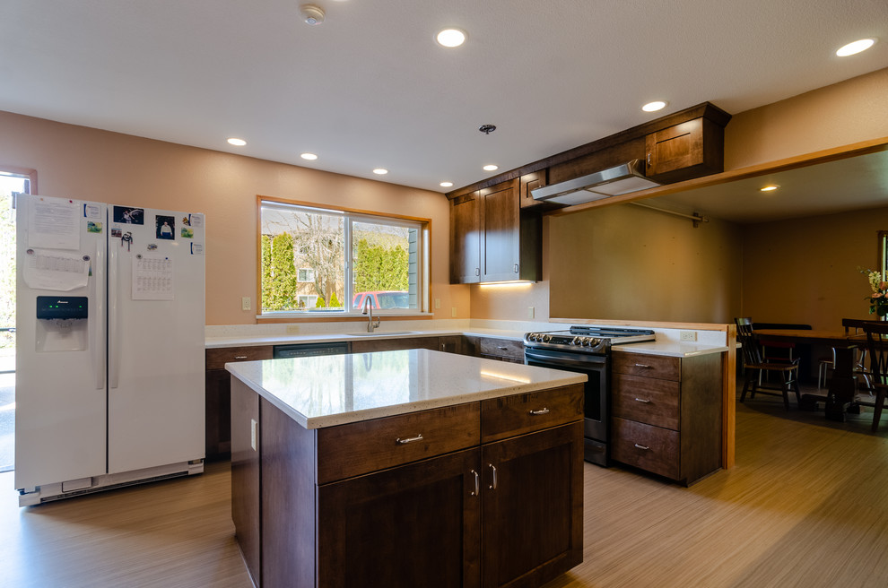 Large transitional u-shaped light wood floor and beige floor enclosed kitchen photo with an undermount sink, recessed-panel cabinets, dark wood cabinets, quartz countertops, stainless steel appliances, an island and white countertops
