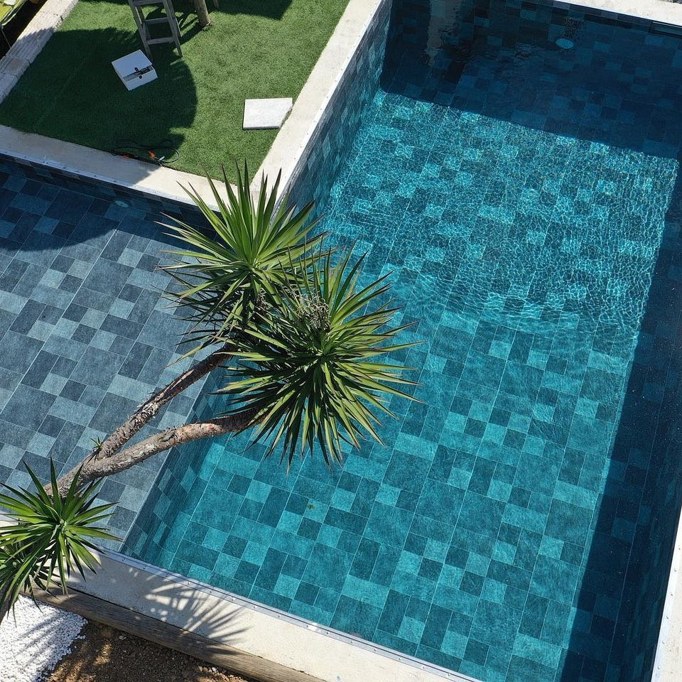 Aménagement d'un grand piscine avec aménagement paysager exotique en L avec des pavés en pierre naturelle.