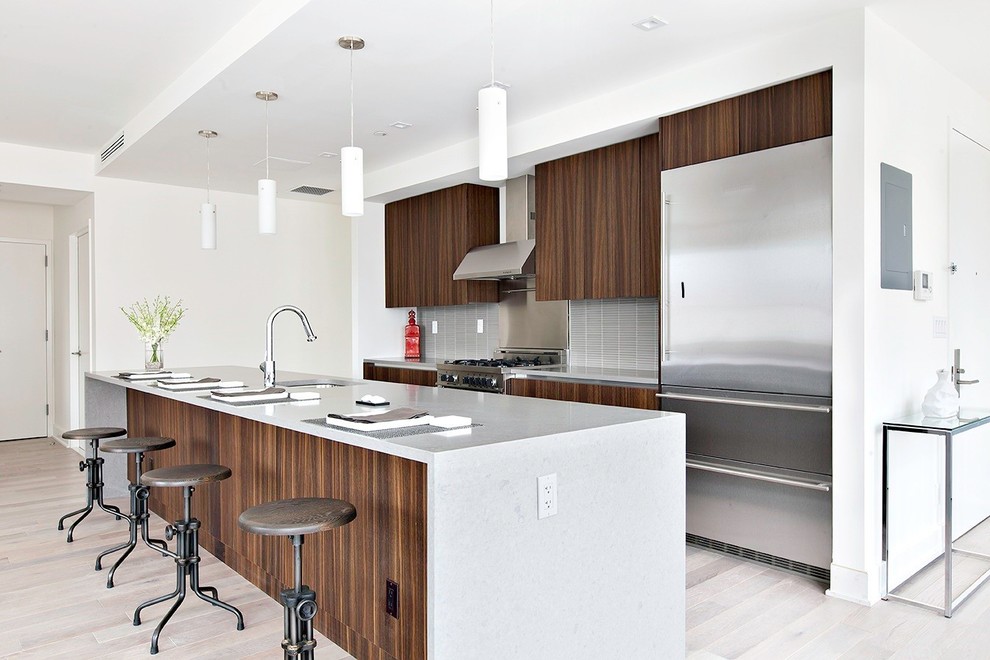 Inspiration for a modern galley light wood floor kitchen remodel in New York with flat-panel cabinets, dark wood cabinets, quartz countertops, gray backsplash, ceramic backsplash and stainless steel appliances