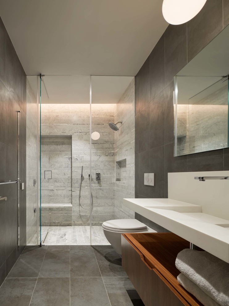 Inspiration for a contemporary bathroom in New York with flat-panel cabinets, medium wood cabinets, a curbless shower, a wall-mount toilet, grey walls, a wall-mount sink, grey floor and a hinged shower door.