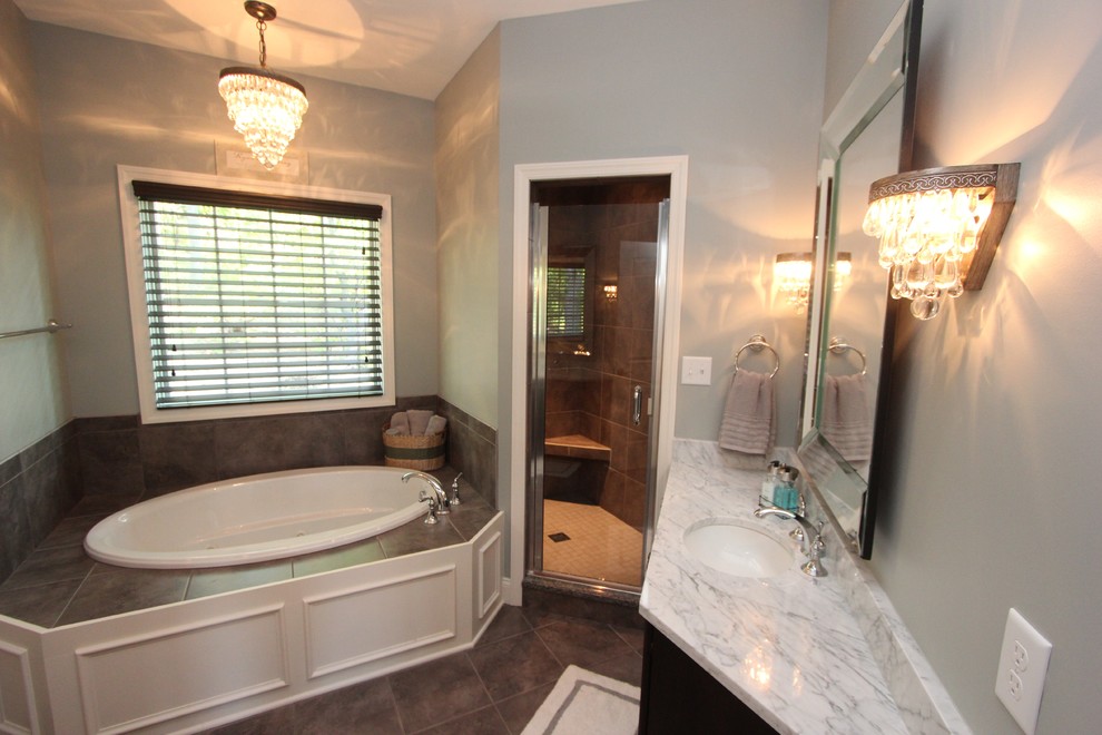 Example of a transitional gray tile and ceramic tile drop-in bathtub design with an undermount sink, marble countertops and a two-piece toilet