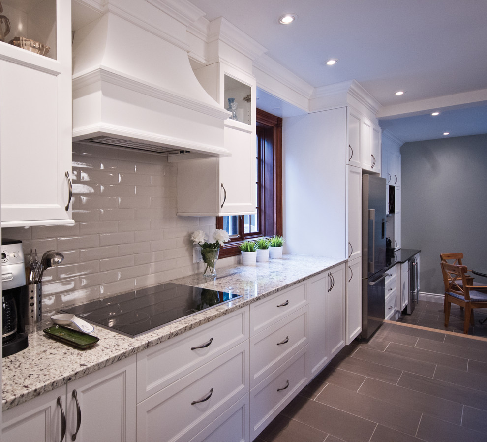 Design ideas for a mid-sized transitional galley eat-in kitchen in Montreal with an undermount sink, shaker cabinets, white cabinets, granite benchtops, beige splashback, subway tile splashback, stainless steel appliances, ceramic floors and with island.