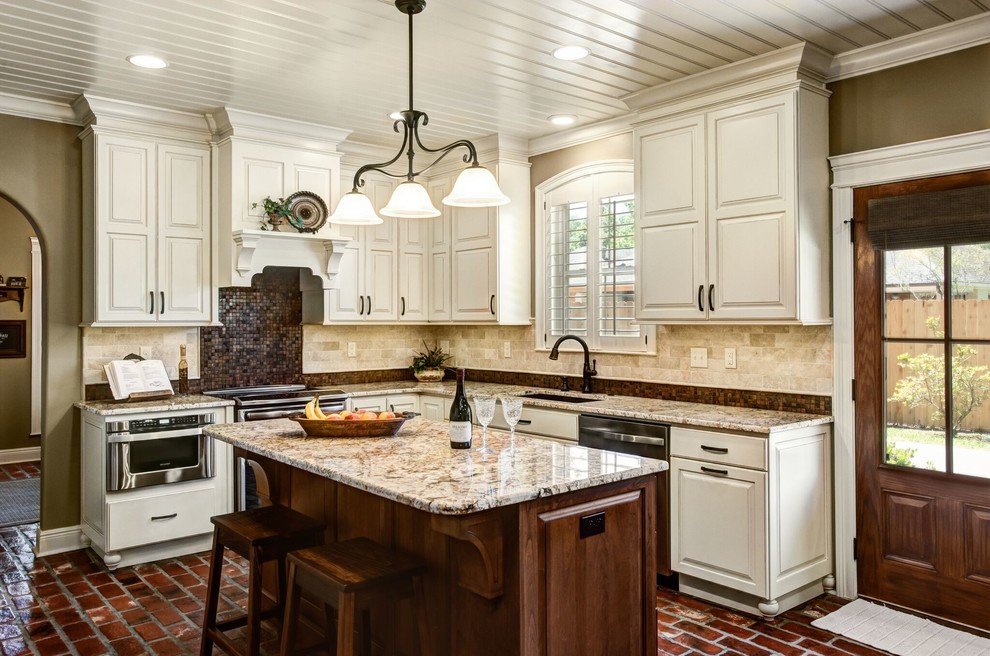 Inspiration for a large traditional l-shaped eat-in kitchen in New Orleans with an undermount sink, raised-panel cabinets, beige cabinets, granite benchtops, brown splashback, travertine splashback, stainless steel appliances, brick floors, with island and red floor.