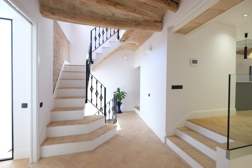 Large country tile l-shaped staircase in Barcelona with metal railing and brick walls.