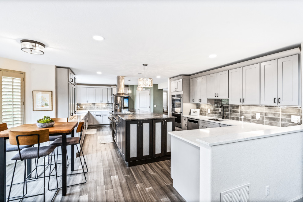 This is an example of a large transitional l-shaped eat-in kitchen in Denver with an undermount sink, shaker cabinets, grey cabinets, granite benchtops, green splashback, ceramic splashback, stainless steel appliances, bamboo floors, with island, brown floor and multi-coloured benchtop.