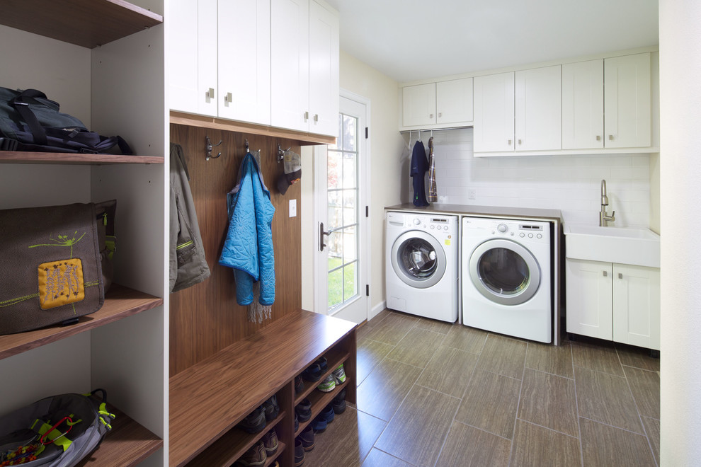 Contemporary laundry room in Denver with a farmhouse sink, white cabinets and brown floor.