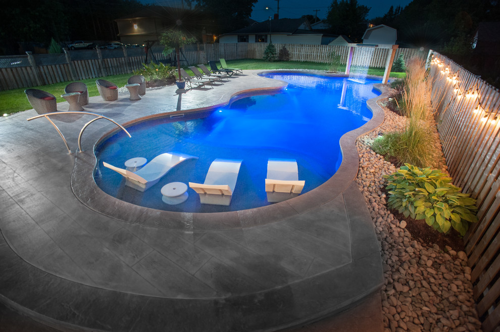 Large beach style side yard custom-shaped natural pool in Other with a pool house and stamped concrete.