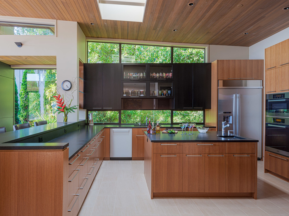 Photo of a midcentury kitchen in Seattle with an undermount sink, flat-panel cabinets, medium wood cabinets, window splashback, stainless steel appliances, with island, beige floor and black benchtop.