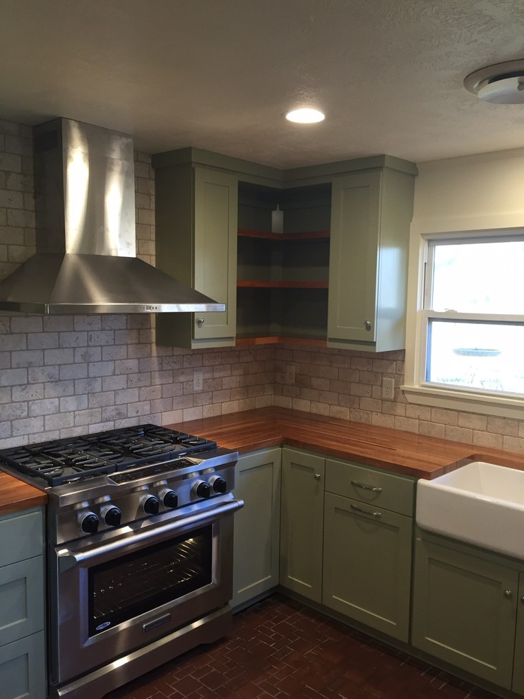 Photo of a large country l-shaped eat-in kitchen in Austin with a farmhouse sink, shaker cabinets, green cabinets, wood benchtops, beige splashback, stone tile splashback and stainless steel appliances.