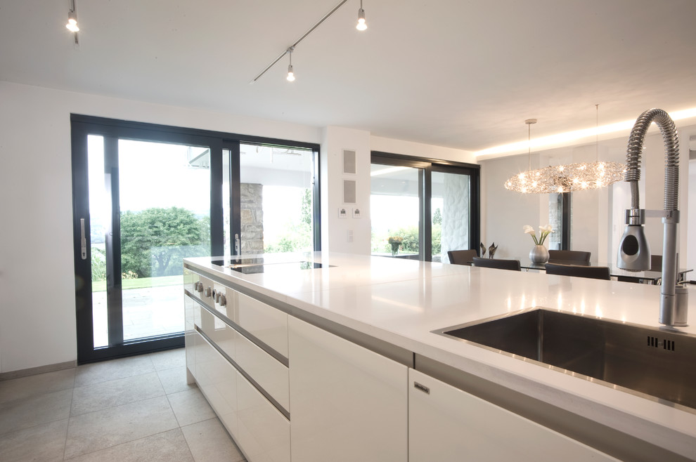 This is an example of a mid-sized contemporary galley open plan kitchen in Nuremberg with a drop-in sink, flat-panel cabinets, white cabinets, solid surface benchtops, mirror splashback, porcelain floors and with island.