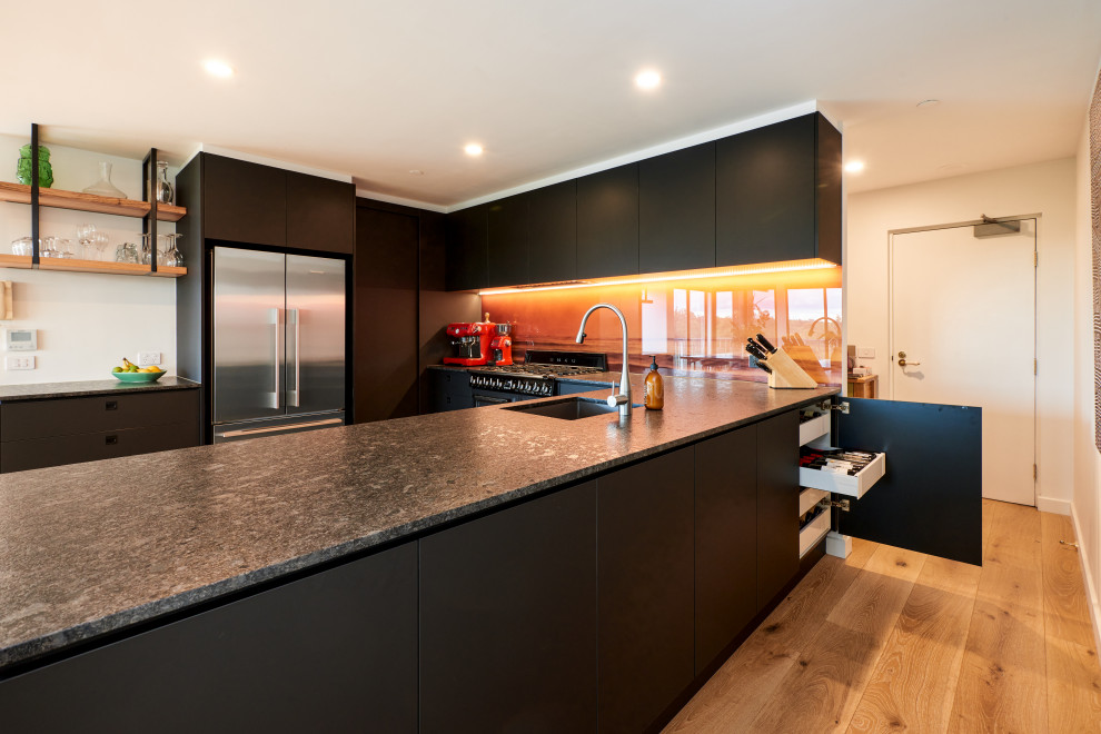 Foto di una cucina minimalista di medie dimensioni con ante lisce, ante nere, top in quarzo composito, paraspruzzi arancione, paraspruzzi con lastra di vetro, elettrodomestici neri e top nero