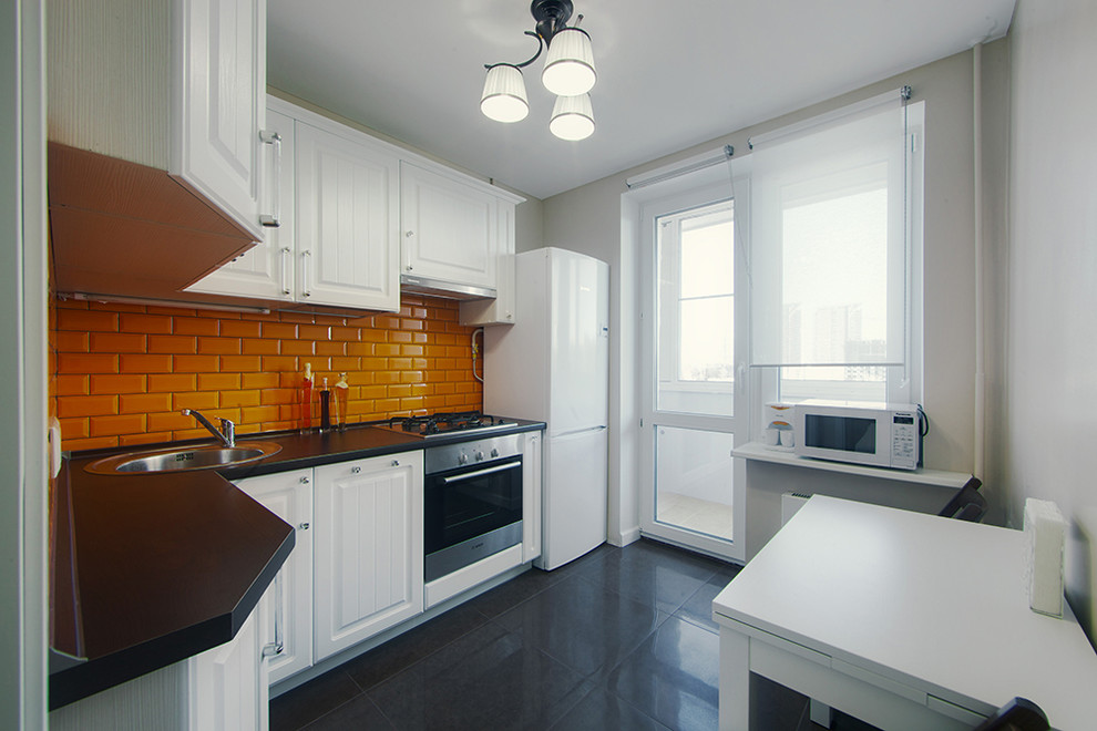 Photo of a contemporary kitchen in Moscow with a drop-in sink, raised-panel cabinets, white cabinets, orange splashback, subway tile splashback, stainless steel appliances, no island and black floor.