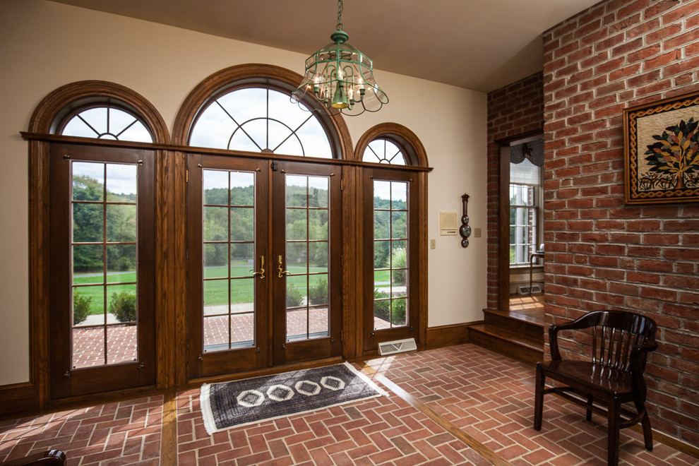 This is an example of a traditional foyer in Philadelphia with brick floors, a double front door and a dark wood front door.