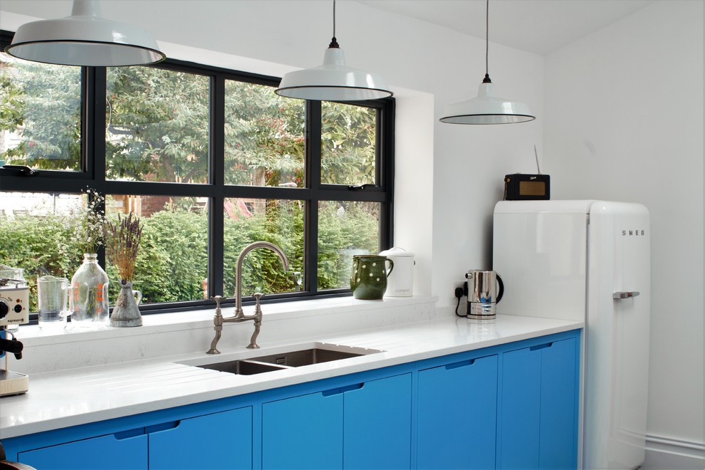 Photo of a small industrial l-shaped separate kitchen in Other with a double-bowl sink, flat-panel cabinets, blue cabinets, quartz benchtops, white splashback, subway tile splashback, black appliances, linoleum floors and a peninsula.