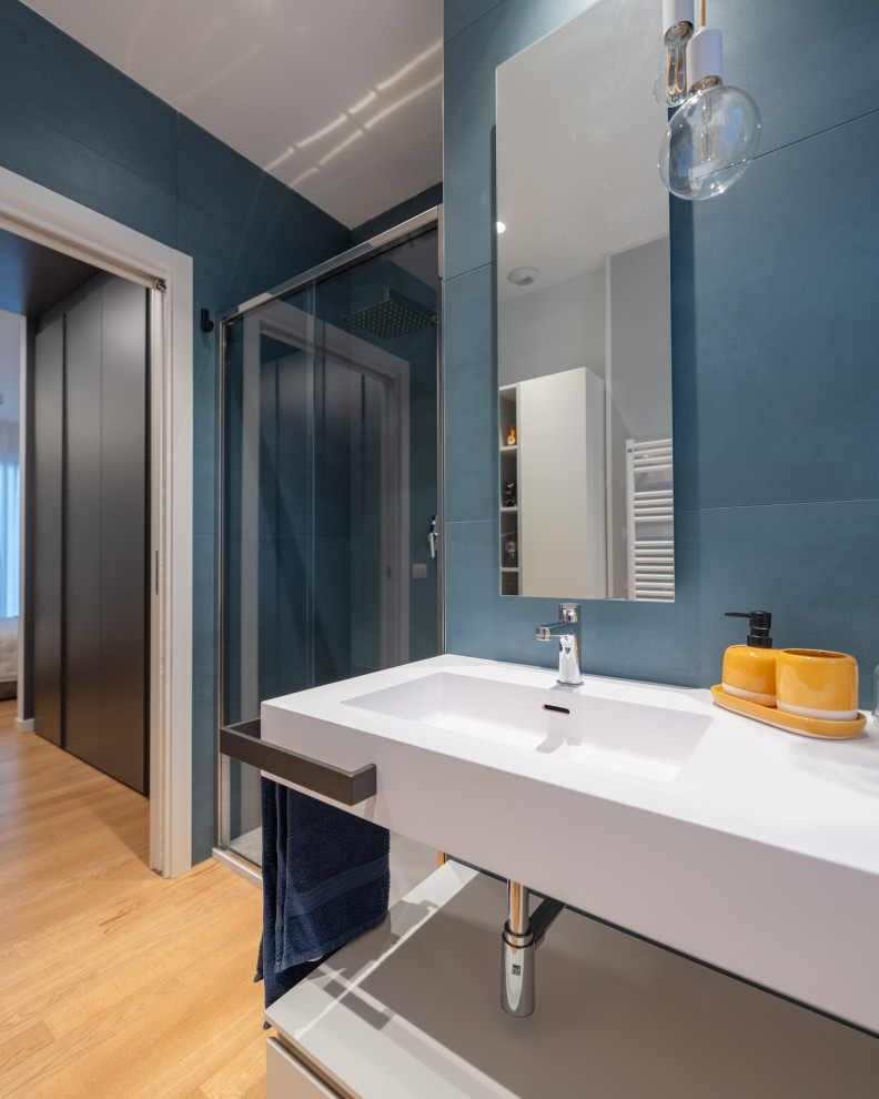 This is an example of a small contemporary master bathroom in Milan with white cabinets, an alcove shower, a two-piece toilet, blue tile, porcelain tile, white walls, light hardwood floors, an integrated sink, solid surface benchtops, beige floor, a sliding shower screen, white benchtops, a single vanity and recessed.