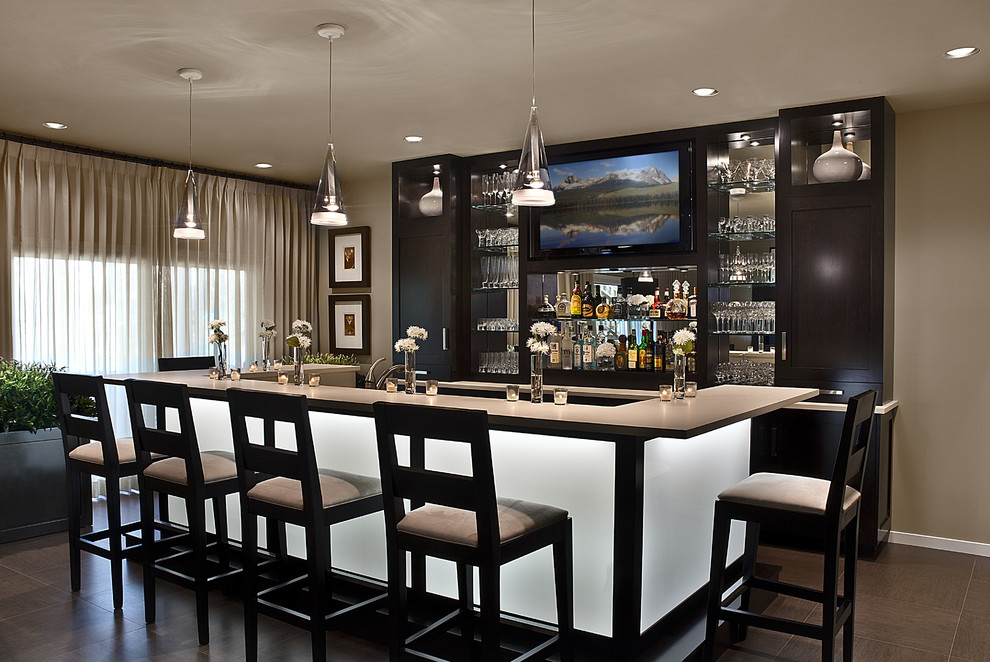 This is an example of a mid-sized contemporary galley seated home bar in Detroit with an undermount sink, shaker cabinets, dark wood cabinets, solid surface benchtops, multi-coloured splashback, mirror splashback and ceramic floors.