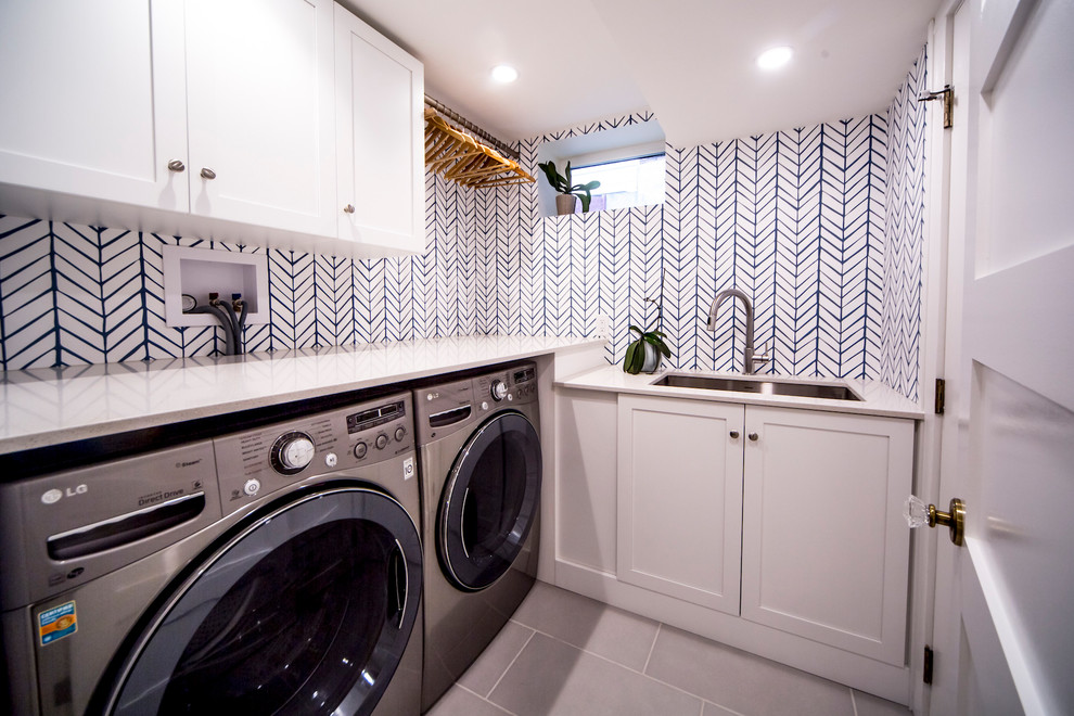 This is an example of a small transitional l-shaped dedicated laundry room in Ottawa with an undermount sink, shaker cabinets, white cabinets, wood benchtops, multi-coloured walls, ceramic floors, a side-by-side washer and dryer and grey floor.