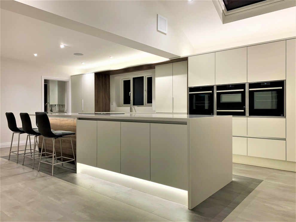 This is an example of a large contemporary single-wall open plan kitchen in Other with an integrated sink, flat-panel cabinets, medium wood cabinets, solid surface benchtops, black appliances, vinyl floors, with island and white benchtop.