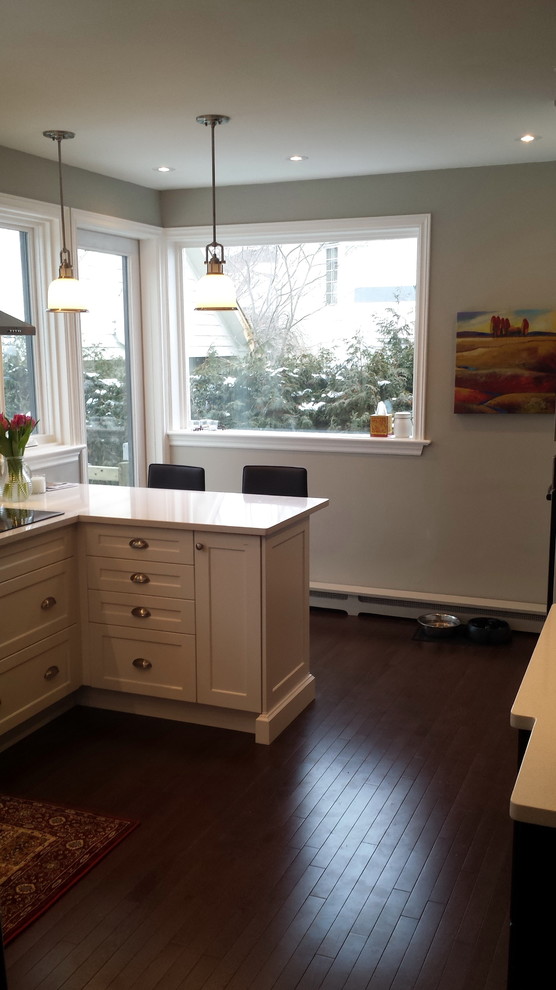 Example of a mid-sized transitional u-shaped dark wood floor enclosed kitchen design in Ottawa with an undermount sink, shaker cabinets, white cabinets, quartz countertops, white backsplash, subway tile backsplash, stainless steel appliances and a peninsula