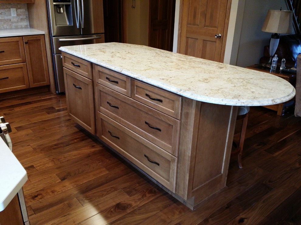 Inspiration for a mid-sized transitional l-shaped medium tone wood floor eat-in kitchen remodel in Milwaukee with an undermount sink, shaker cabinets, medium tone wood cabinets, granite countertops, beige backsplash, stone tile backsplash, stainless steel appliances and an island