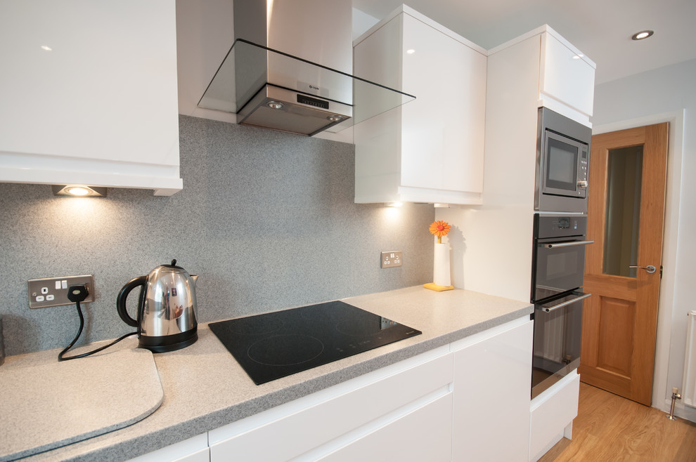 This is an example of a large contemporary eat-in kitchen in Sussex with a drop-in sink, flat-panel cabinets, solid surface benchtops, grey splashback, stainless steel appliances, no island and grey benchtop.