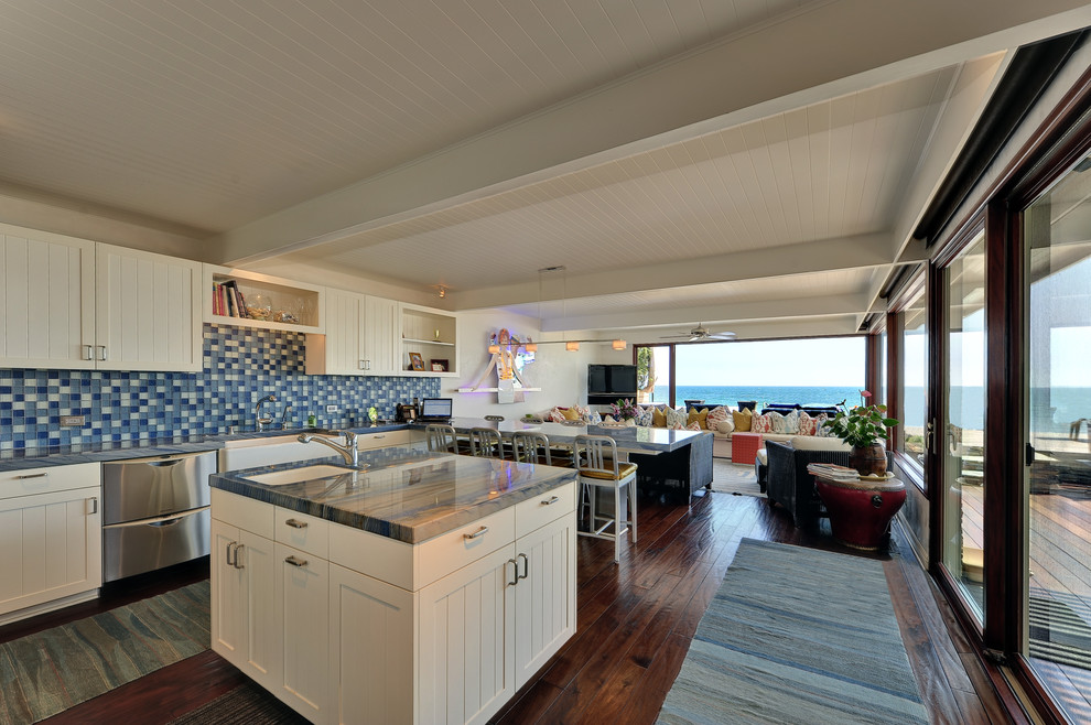 Beach style l-shaped open plan kitchen in Los Angeles with white cabinets and blue splashback.