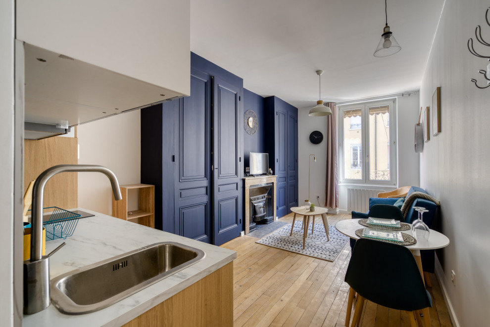 Cette image montre une petite salle de séjour minimaliste ouverte avec un mur bleu, parquet clair, une cheminée standard, un manteau de cheminée en pierre de parement et un téléviseur indépendant.