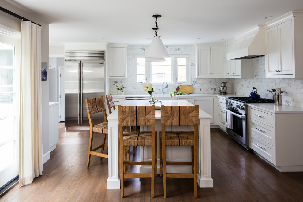 Mid-sized transitional l-shaped open plan kitchen in Seattle with a farmhouse sink, shaker cabinets, white cabinets, quartz benchtops, white splashback, marble splashback, stainless steel appliances, medium hardwood floors, with island and brown floor.
