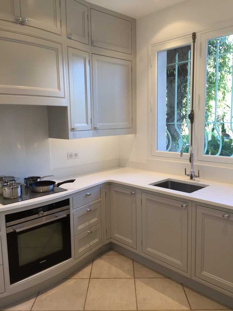 Small traditional l-shaped separate kitchen in Other with a single-bowl sink, beaded inset cabinets, grey cabinets, solid surface benchtops, white splashback, black appliances, no island and grey floor.