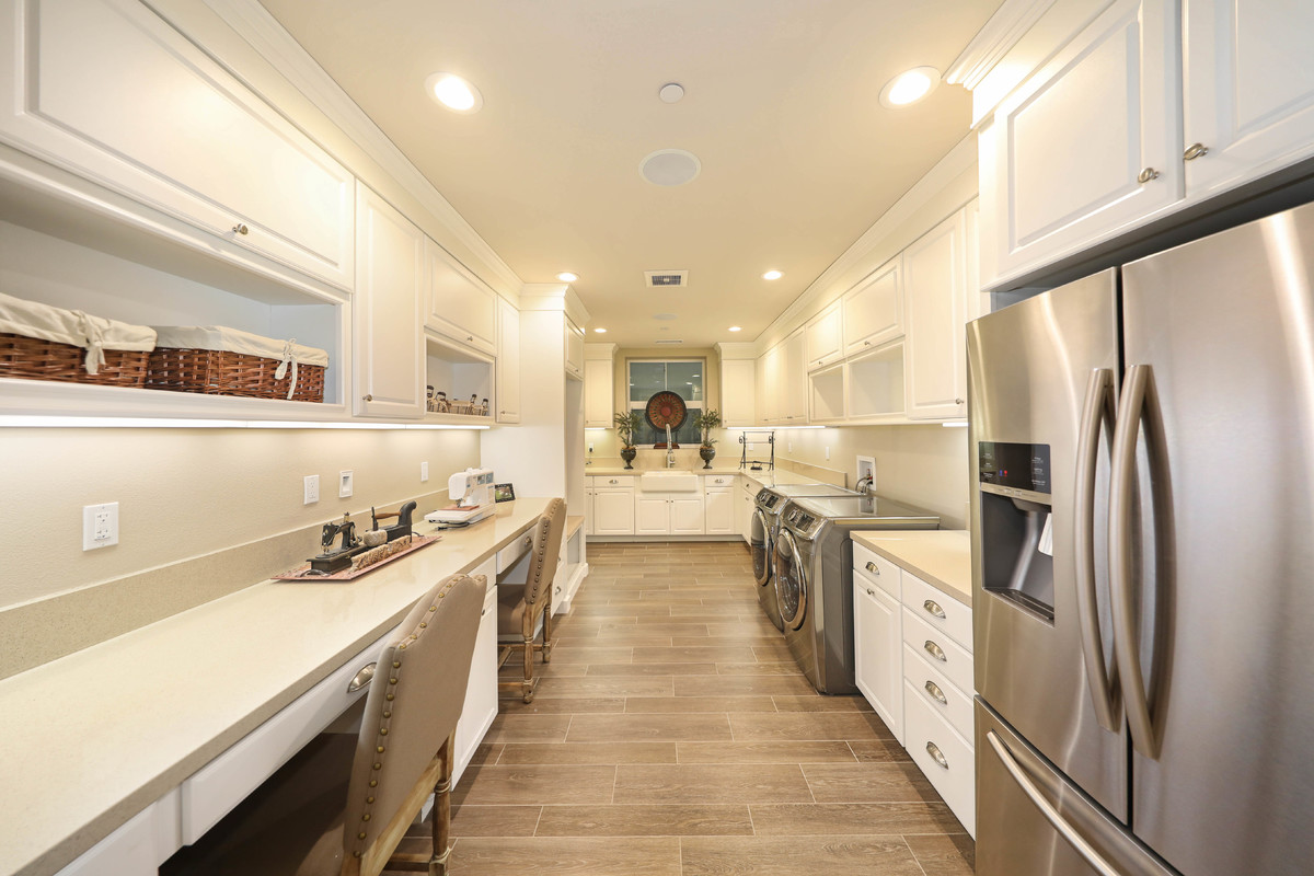 Large transitional u-shaped kitchen in Orange County with a farmhouse sink, raised-panel cabinets, white cabinets, solid surface benchtops, porcelain floors and brown floor.