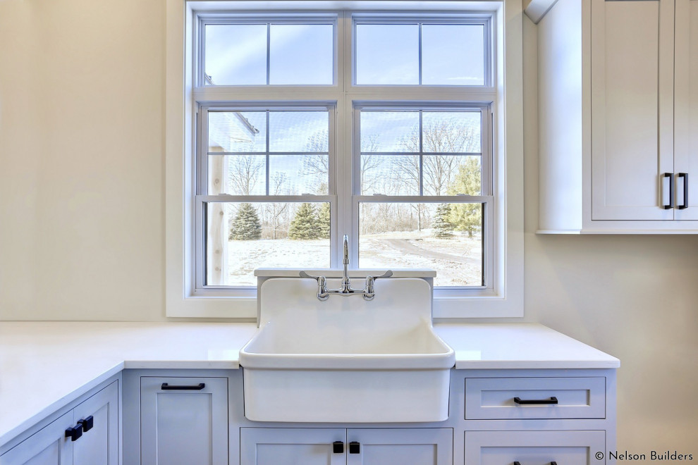 Photo of a mid-sized country l-shaped dedicated laundry room in Chicago with a farmhouse sink, shaker cabinets, grey cabinets, quartz benchtops, white walls, ceramic floors, a side-by-side washer and dryer and white benchtop.