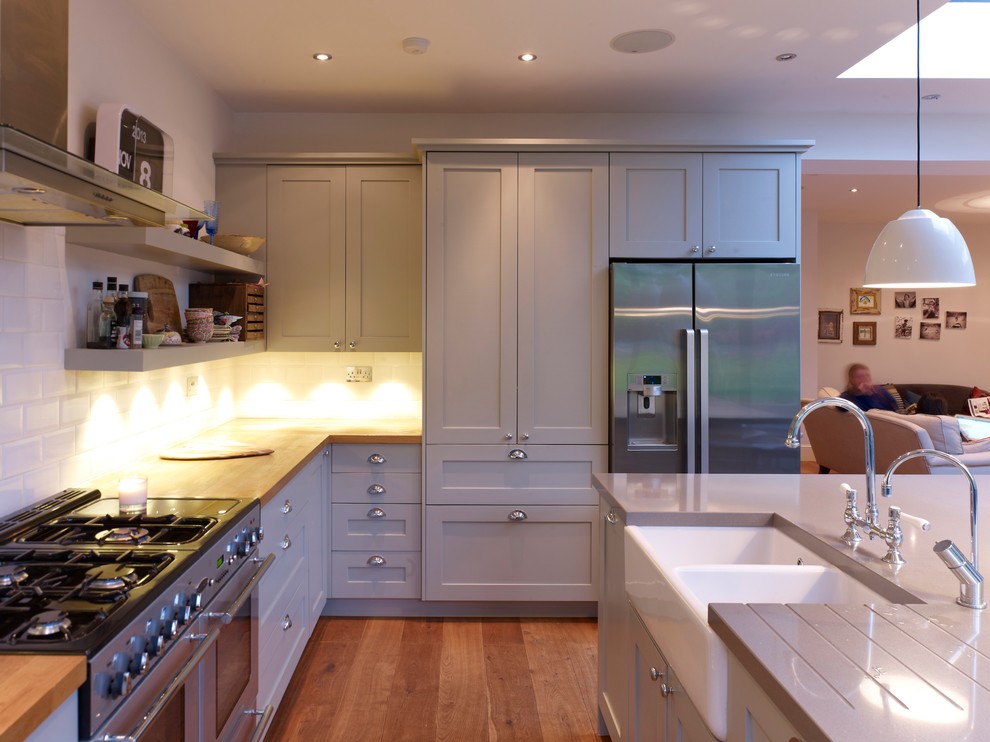 Inspiration for a contemporary kitchen in London with recessed-panel cabinets, white splashback, subway tile splashback, stainless steel appliances, light hardwood floors and with island.