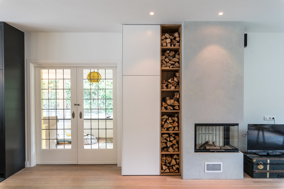 This is an example of a mid-sized contemporary open concept family room in Amsterdam with grey walls, light hardwood floors, a corner fireplace, a concrete fireplace surround, a freestanding tv and beige floor.