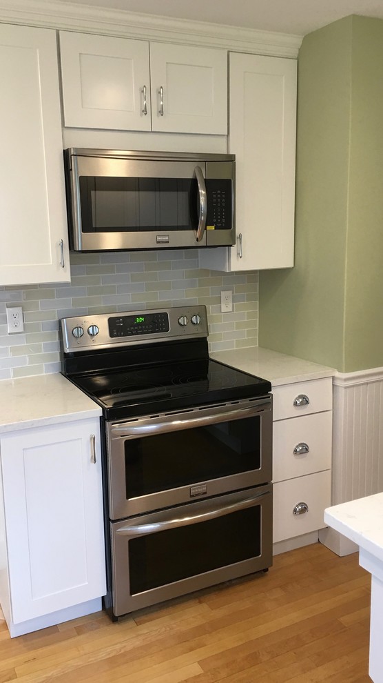 Inspiration for a mid-sized light wood floor enclosed kitchen remodel in Boston with flat-panel cabinets, white cabinets, white backsplash, glass tile backsplash, stainless steel appliances and white countertops